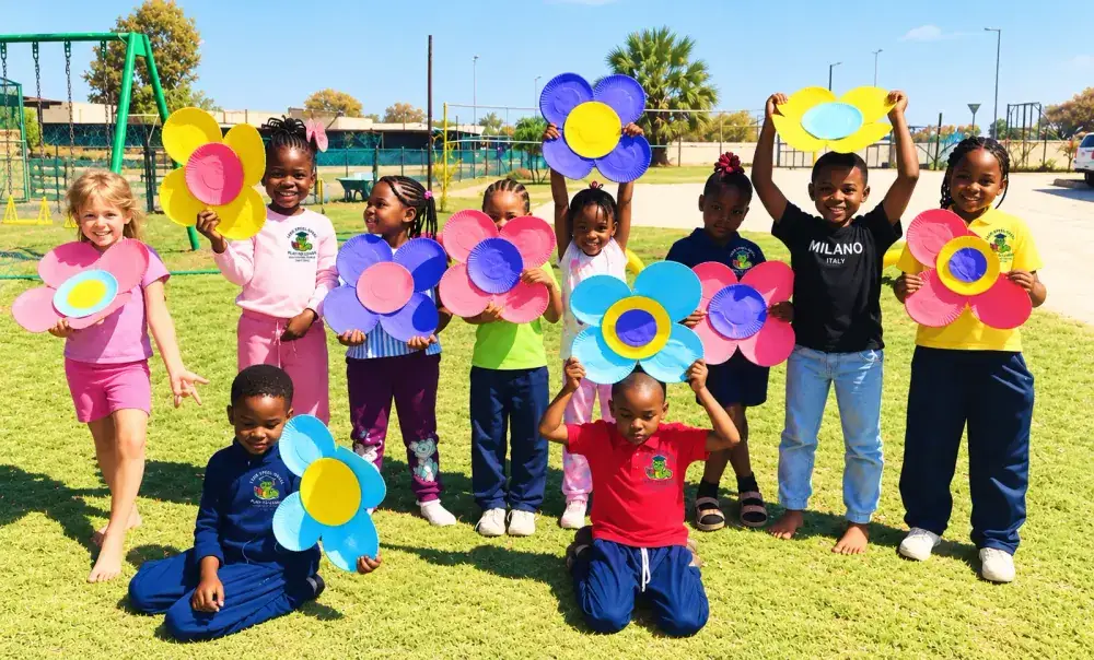 Children on the school lawn holding up big paper-plate flowers they made.