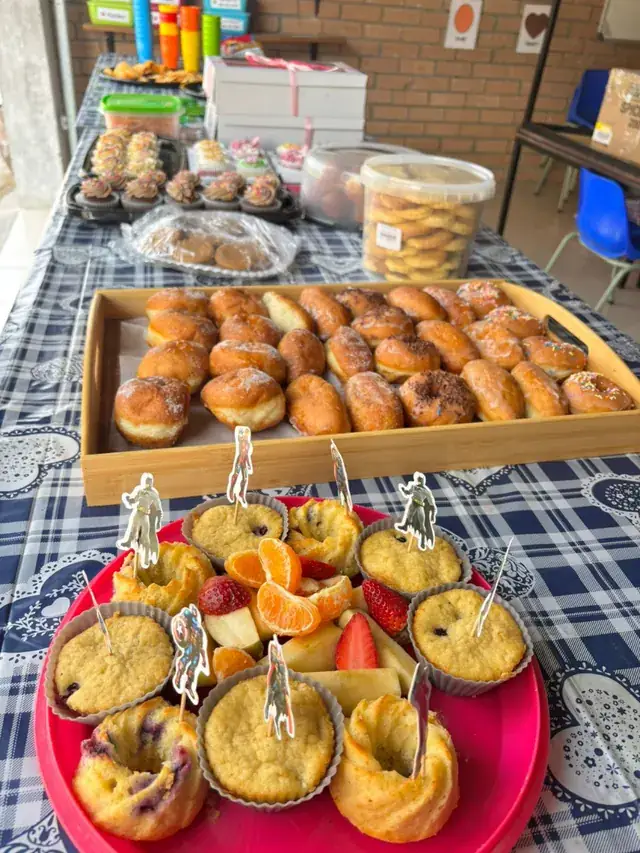 A party table with doughnuts, muffins and a fruit platter.