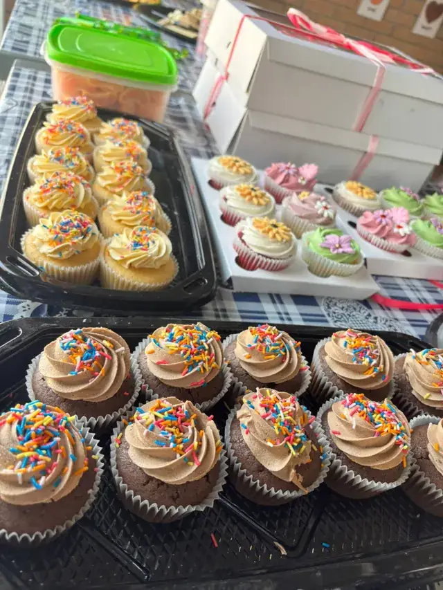 Trays of cupcakes with sprinkles and icing flowers on a party table.