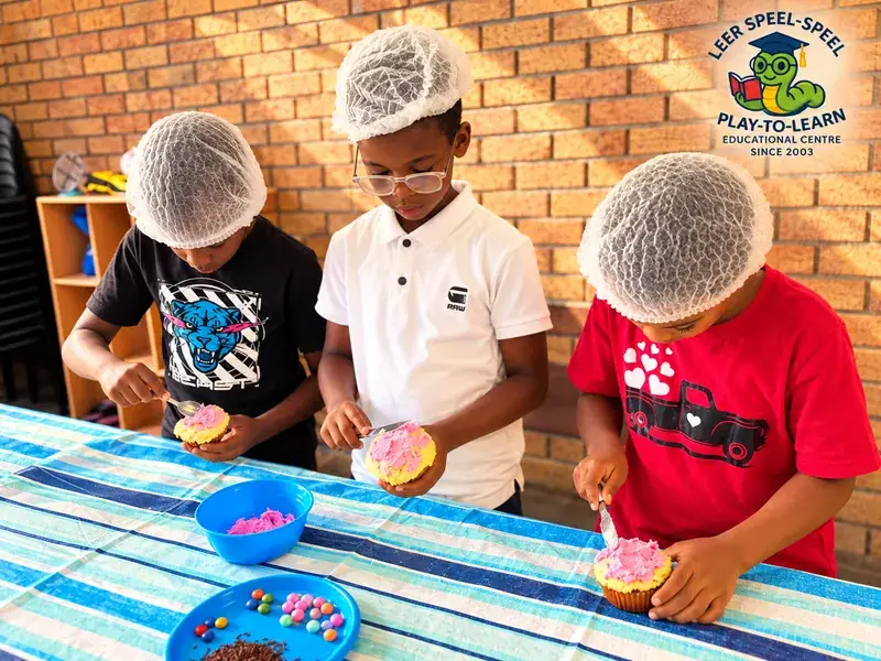 Three children in hair nets icing and decorating cupcakes.