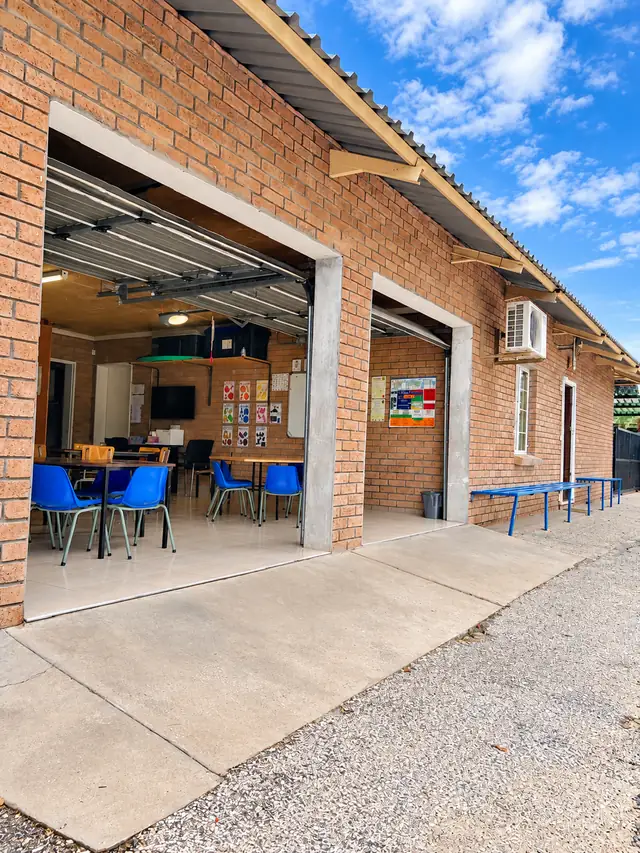 The brick classroom block at our Okatana campus, with its wide doors open onto blue chairs and tables.