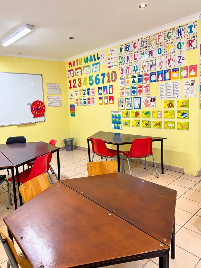 A yellow classroom with a maths wall, alphabet posters and red chairs at our Okatana campus.