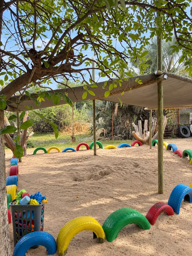 A shaded sandpit ringed with painted tyres and a basket of toys at our Okatana campus.