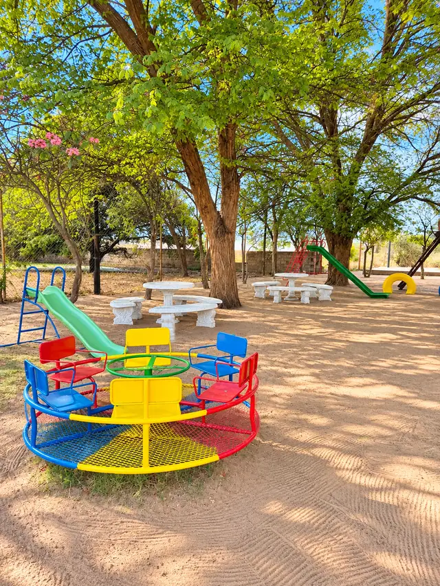 A colourful merry-go-round and slide in the shade of tall trees at our Okatana campus.