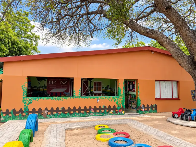 The orange classroom building at our Ongwediva campus, with painted tyres and toy cars in the front play area.