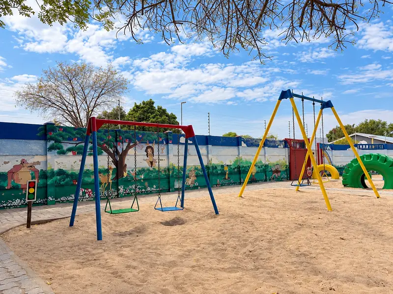 Blue and yellow swings in the sandpit, in front of a painted mural wall at our Ongwediva campus.