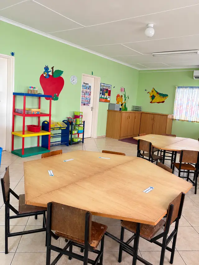 A bright green classroom with wooden tables, toy shelves and an apple mural at our Ongwediva campus.