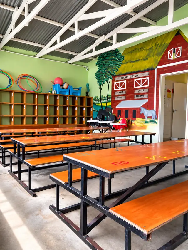 Long wooden tables and benches in a hall with a red barn mural at our Ongwediva campus.