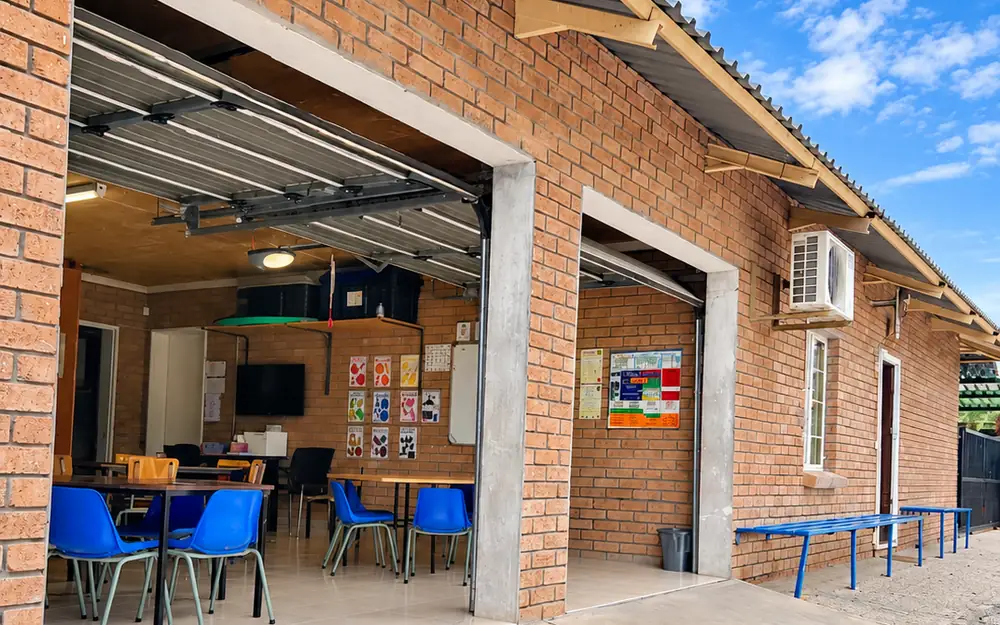 The brick classroom block at our Okatana campus, with its wide doors open onto blue chairs and tables.